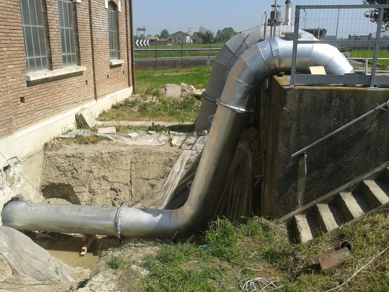 Un grosso tubo esce dal terreno davanti a un edificio in mattoni