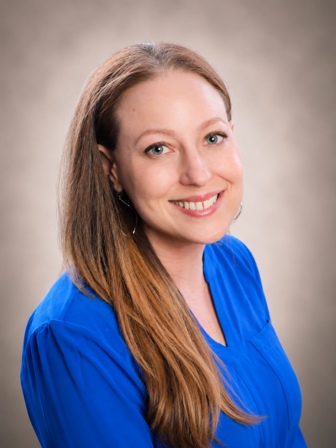 Smiling person in a bright blue blouse against a soft gray studio background