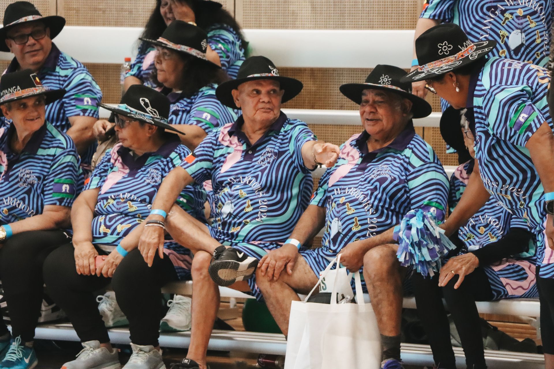 A group of people are sitting on a bench wearing hats and shirts.