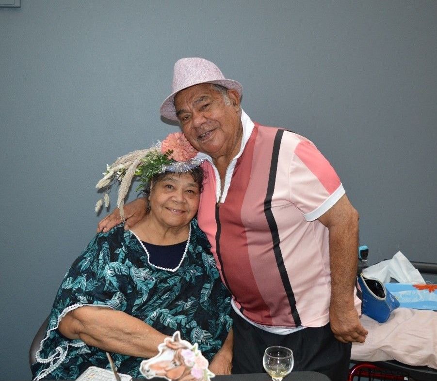 A man and a woman are posing for a picture . the woman is wearing a hat with flowers on it.