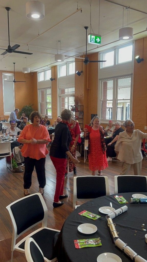 A group of people are dancing in a room with tables and chairs.