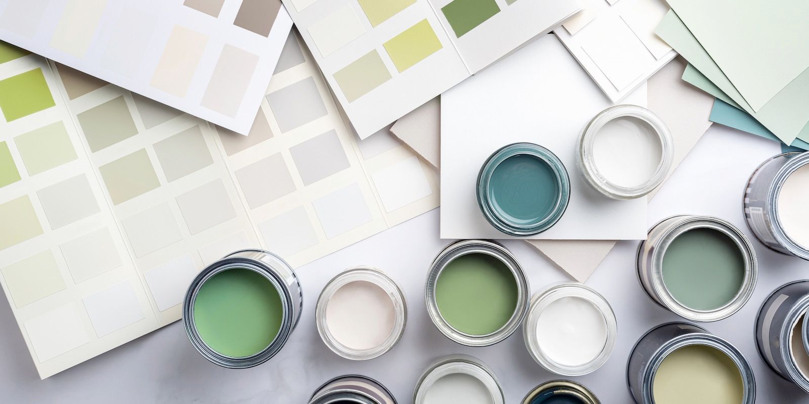 Paint cans in various shades of green and white, with paint swatch cards on a white surface.