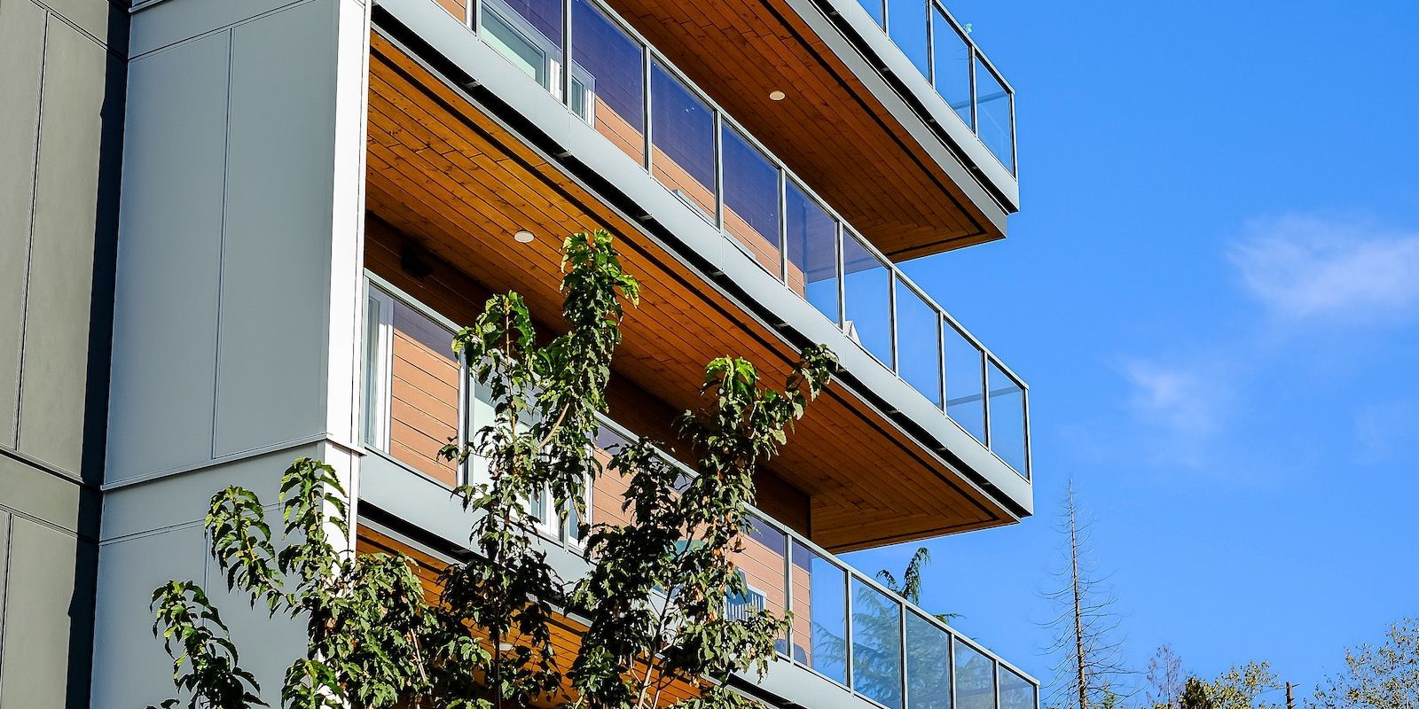 Modern building with wooden balconies and glass railings against a blue sky.