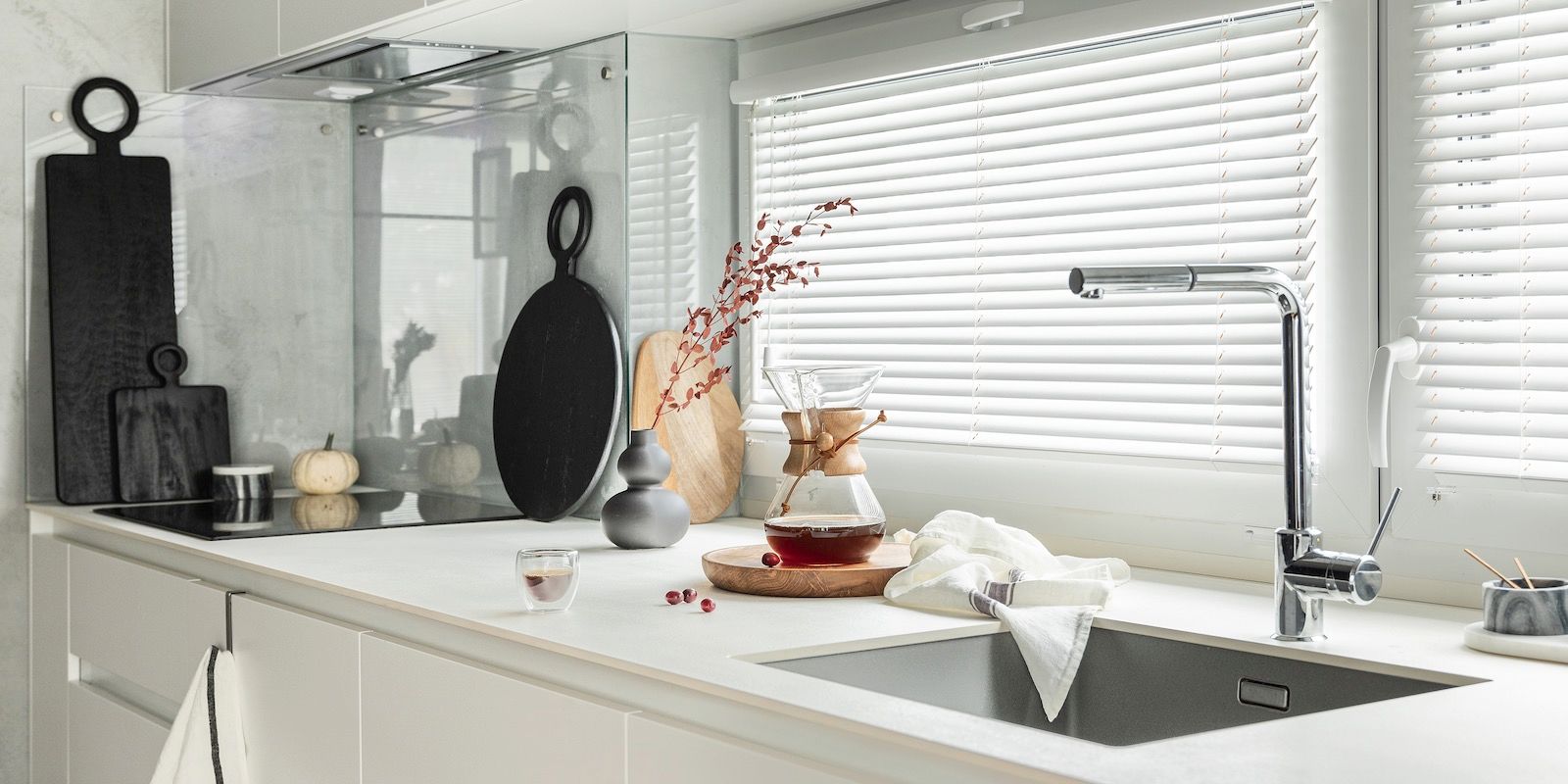 Kitchen counter with sink, faucet, cutting boards, and window with blinds.