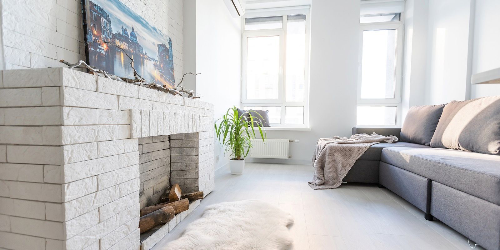 Cozy living room with white brick fireplace, gray couch, and large windows.