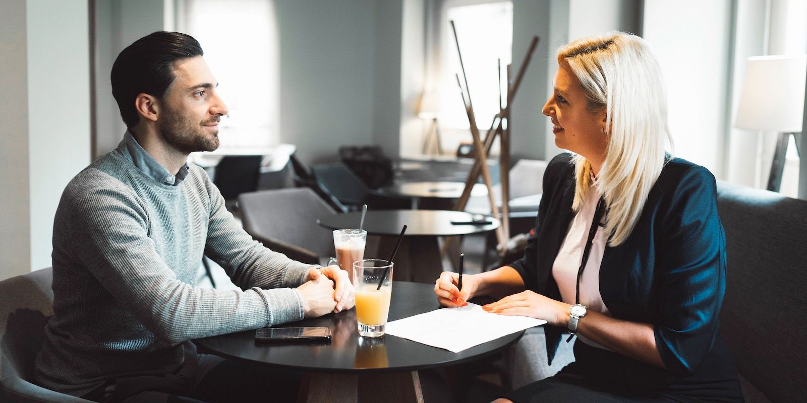 Man and woman seated at a table in a cafe, discussing documents, drinks present.