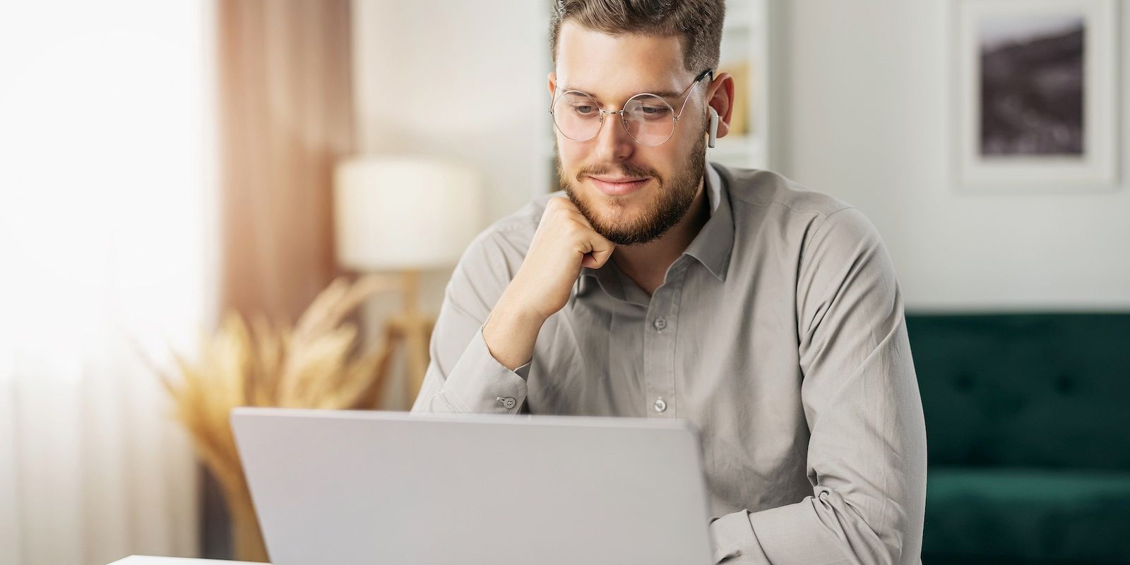Man with glasses, working on a laptop in a home office.