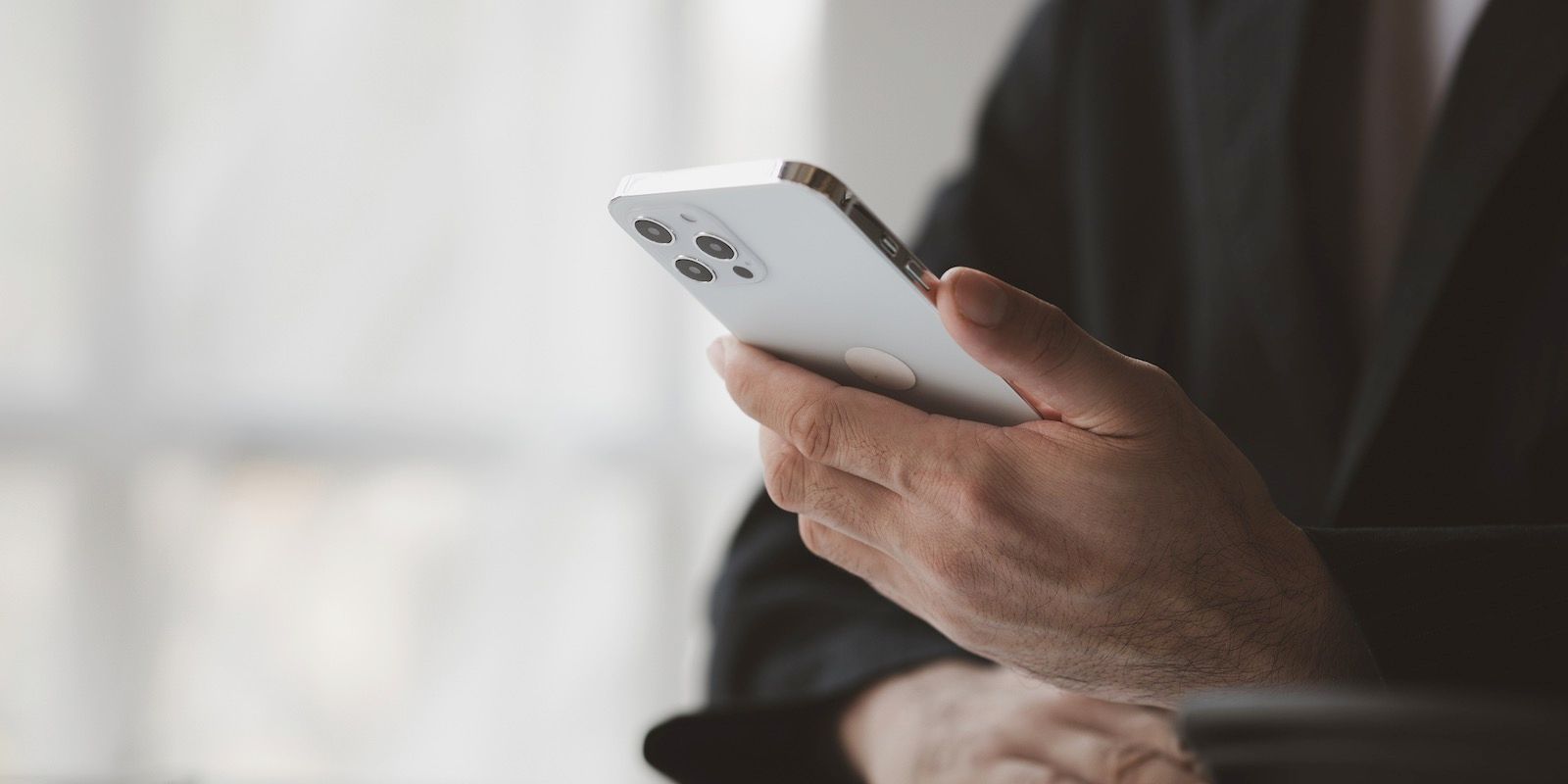 A person in a black suit holding a white cell phone with their right hand.