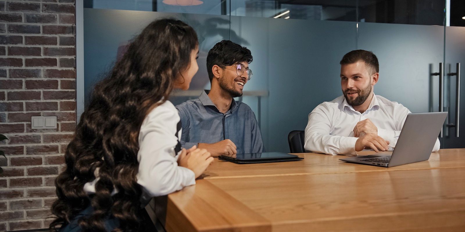 Three people smiling and sitting at a wooden table in an office setting.