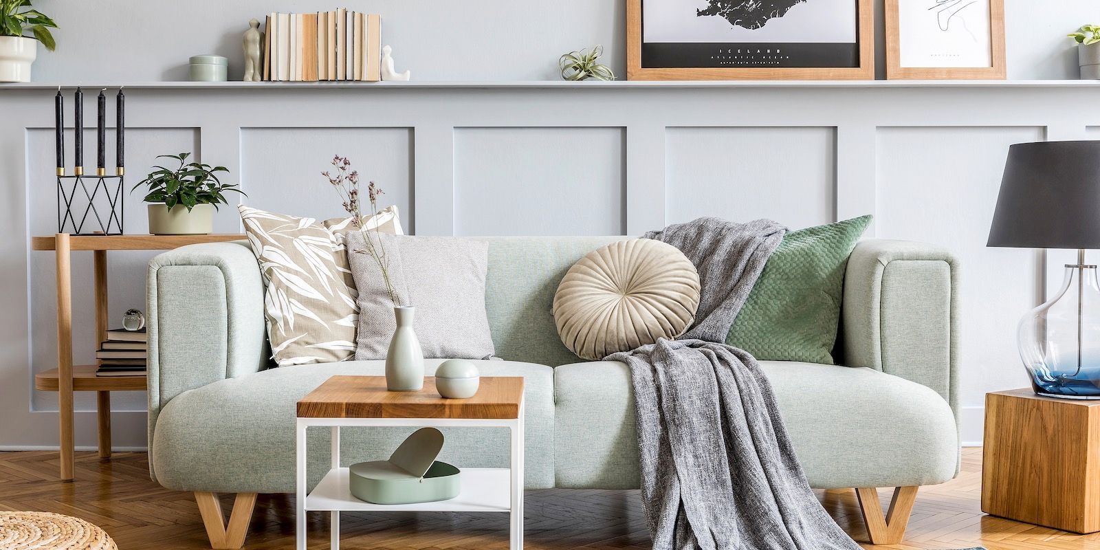A cozy living room with a sage green sofa, wooden tables, and decorative pillows.