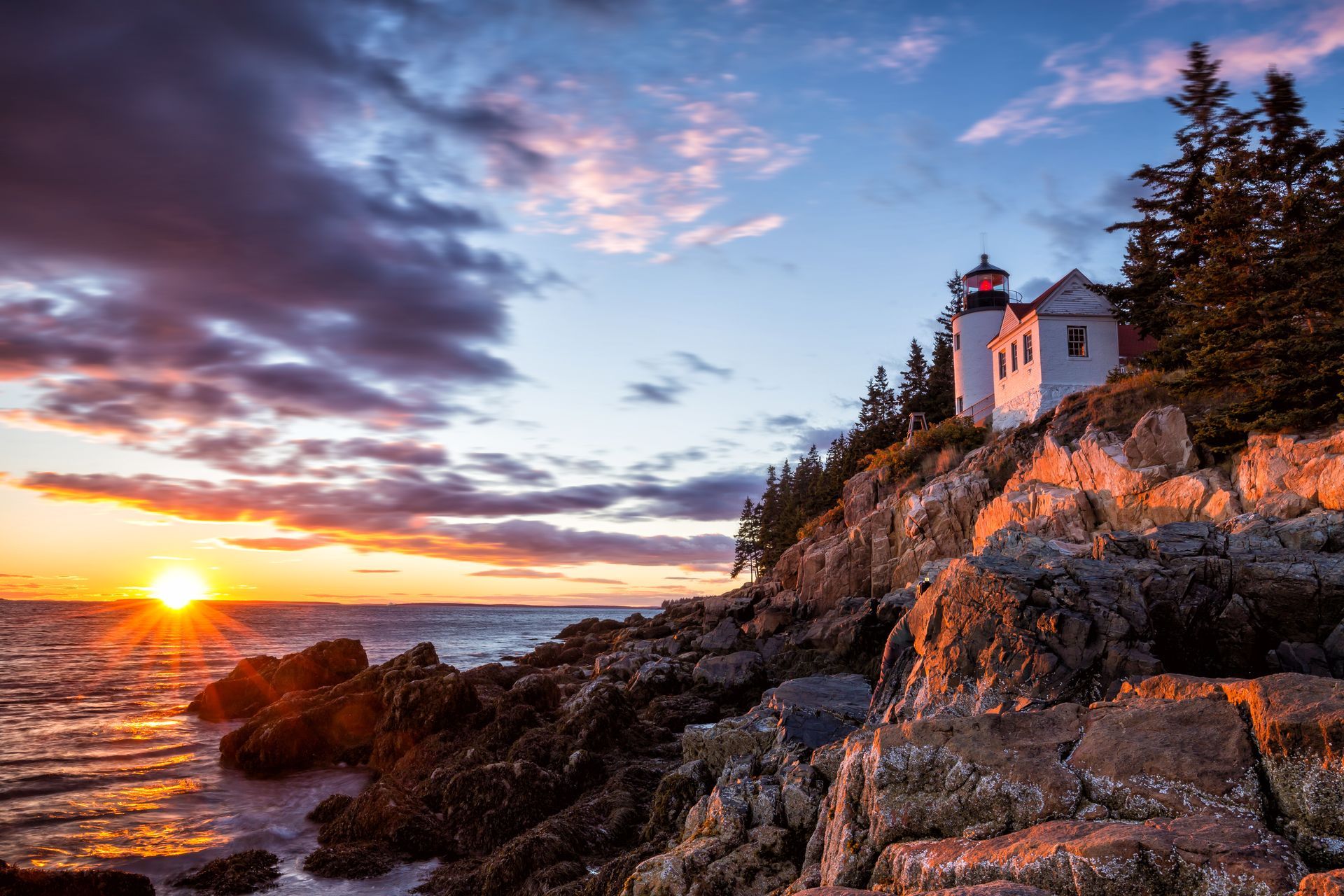 A lighthouse is sitting on top of a rocky cliff overlooking the ocean at sunset.