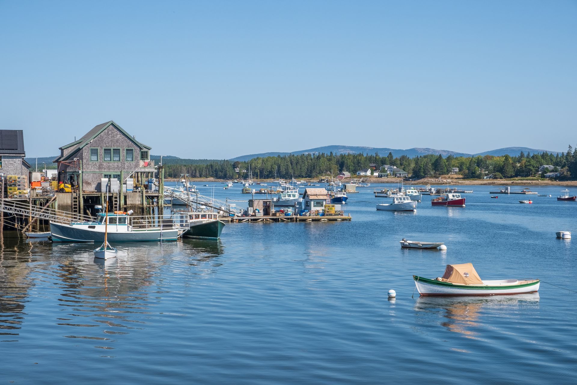 Coastal scene with boats in the water, a weathered building on a pier, and a clear blue sky.