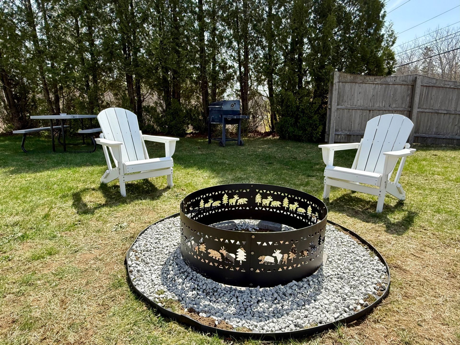 Two white chairs are sitting next to a fire pit in a backyard.