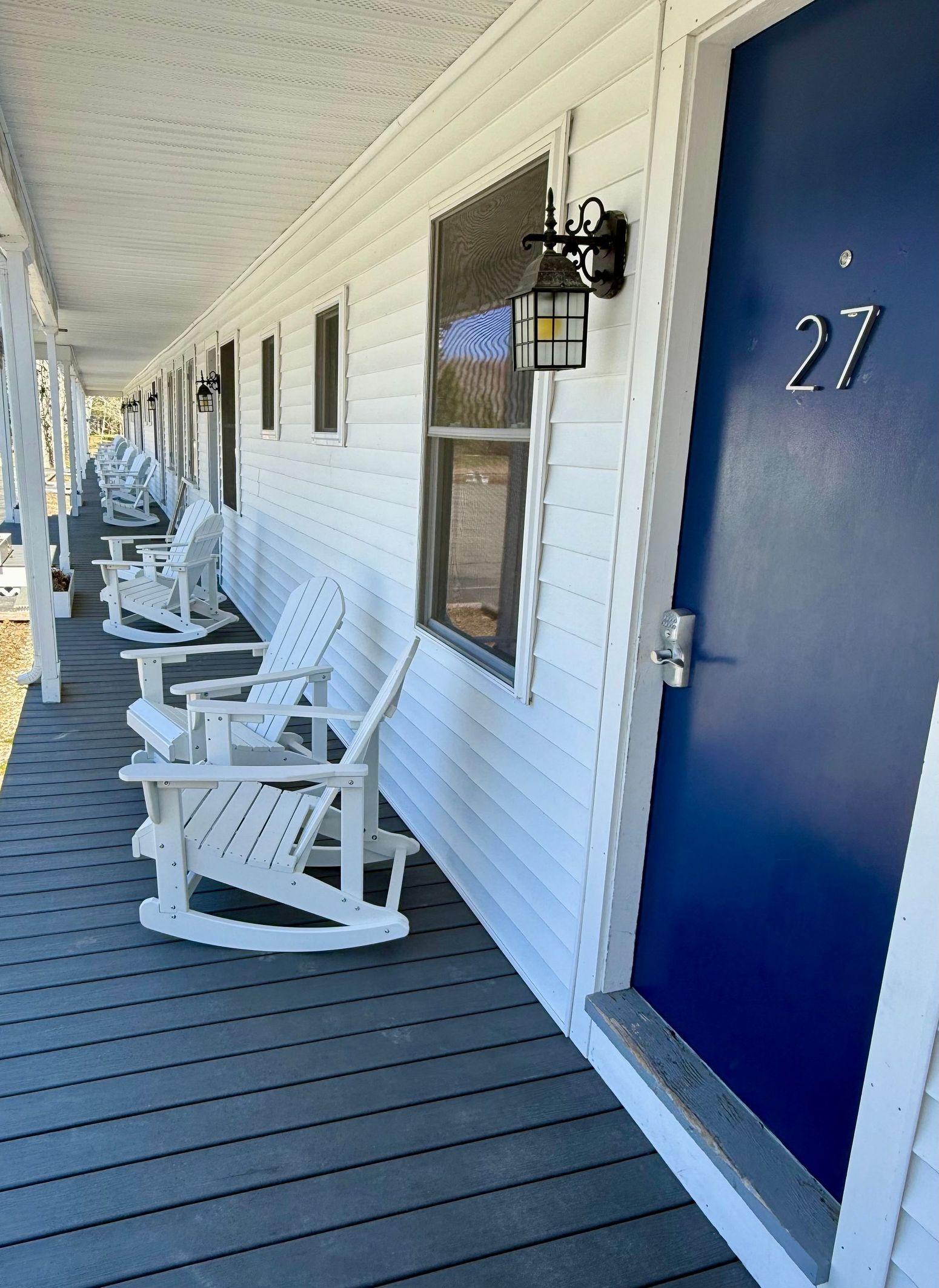 Exterior of a motel hallway with white rocking chairs, blue doors, and a covered porch.