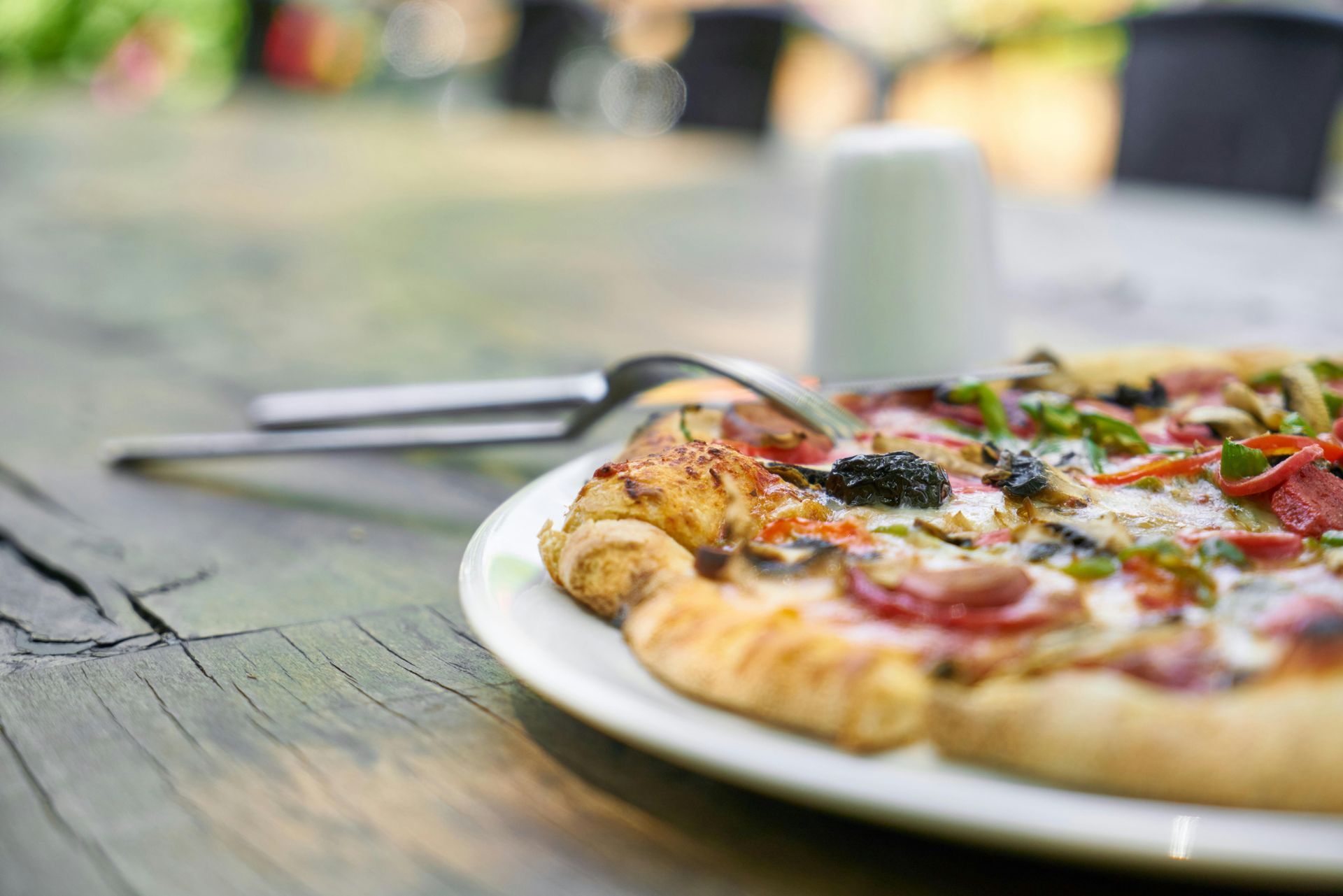 A pizza on a white plate with a fork on a wooden table.