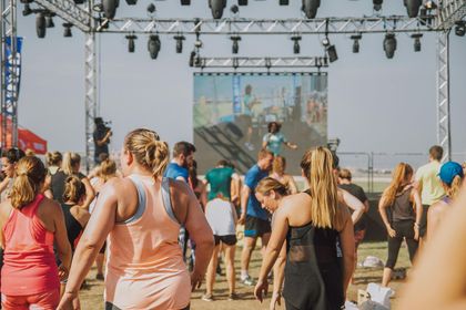A group of people exercising in front of a stage with a large screen during an outdoor fitness event.