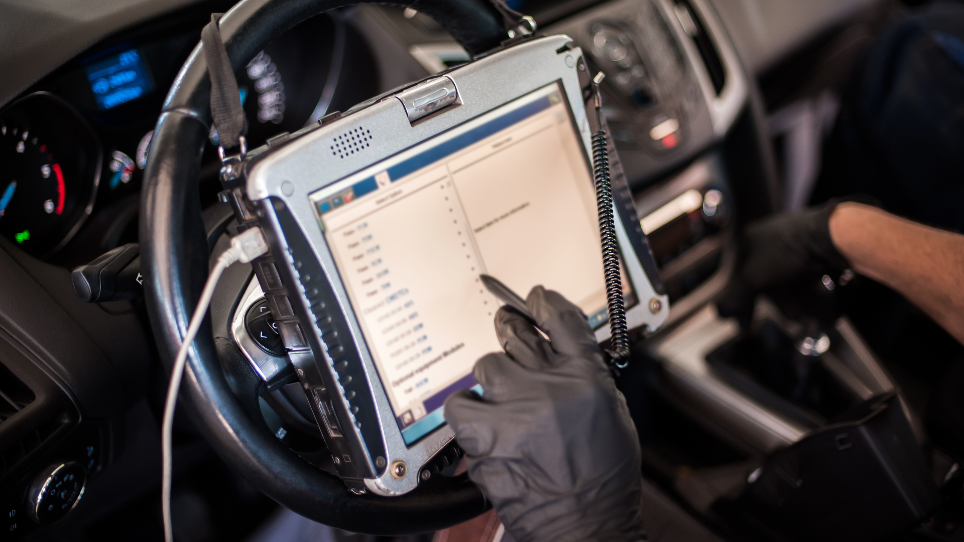 Mechanic using a diagnostic tablet connected to a car's steering wheel, displaying a waveform chart for troubleshooting.