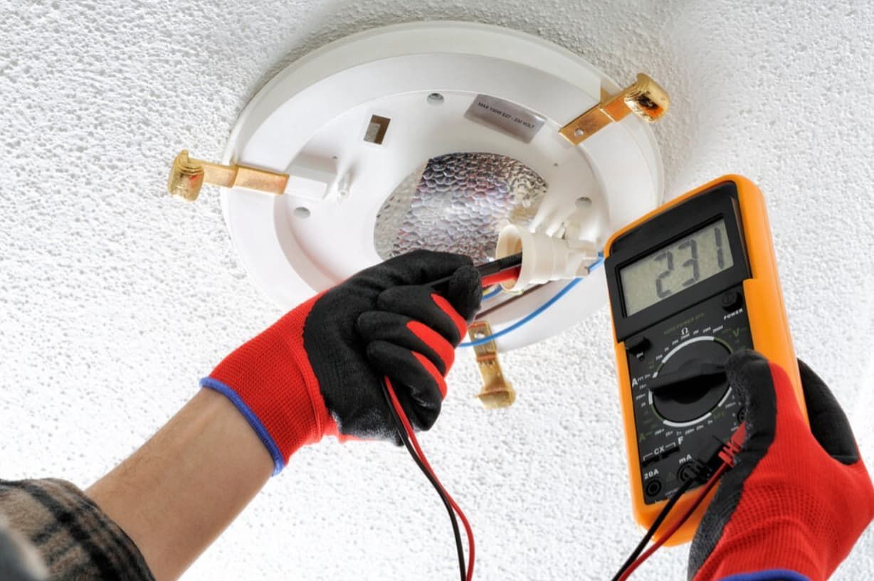 A Man Is Using A Digital Multimeter To Test A Light Bulb — Mozzlec Electrical & Airconditioning In Urangan, QLD