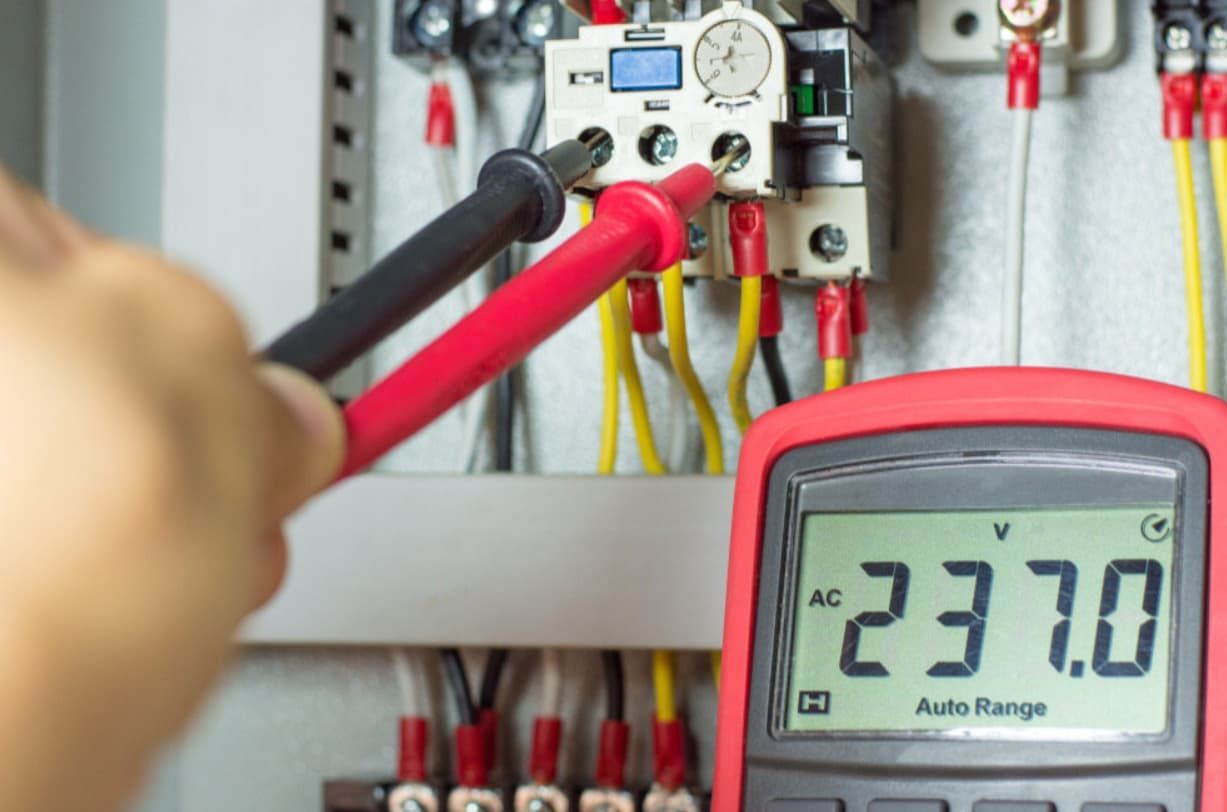 A Person Is Using A Multimeter To Measure Voltage In An Electrical Box — Mozzlec Electrical & Airconditioning In Urangan, QLD