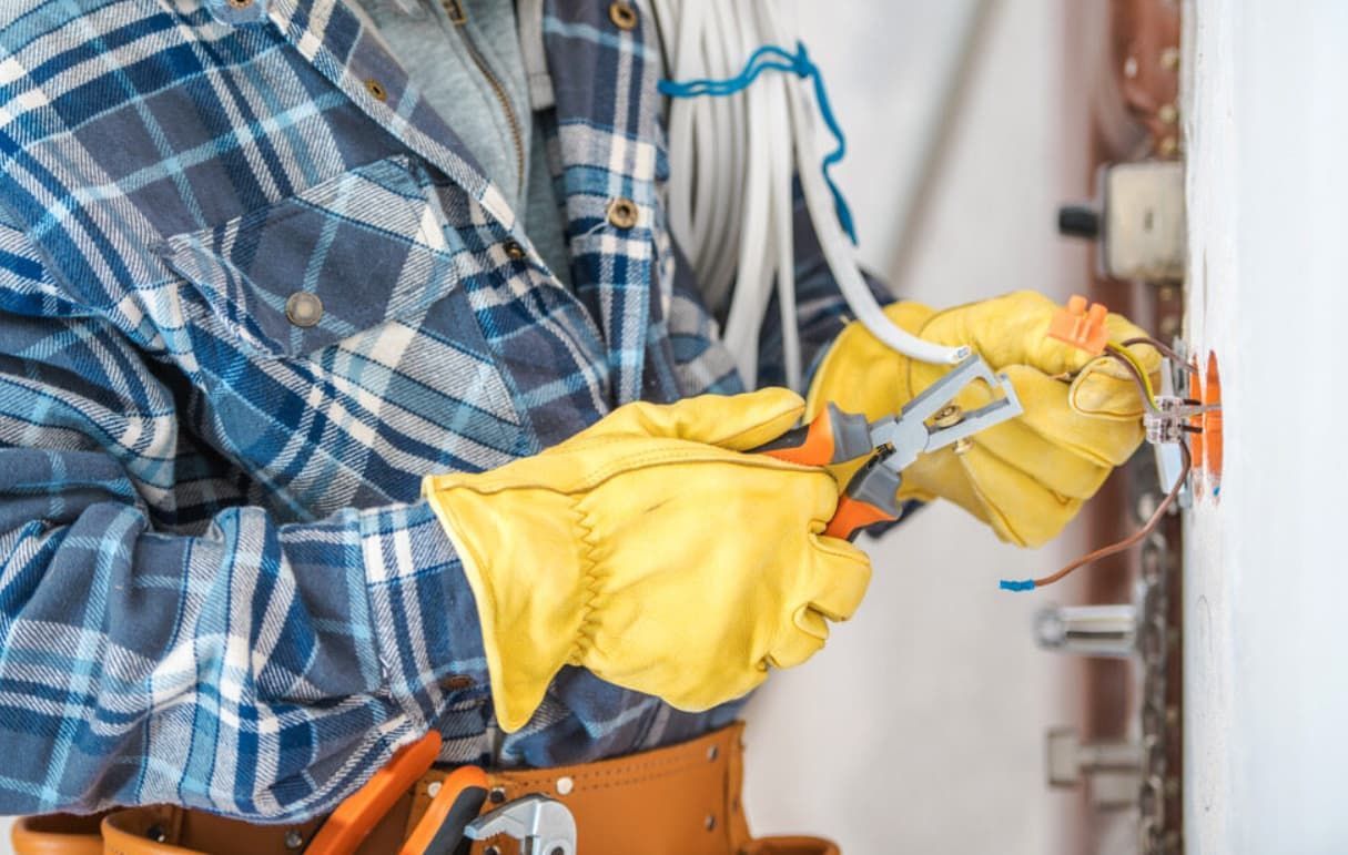 An Electrician Is Working On A Wall With A Pair Of Pliers — Mozzlec Electrical & Airconditioning In Urangan, QLD
