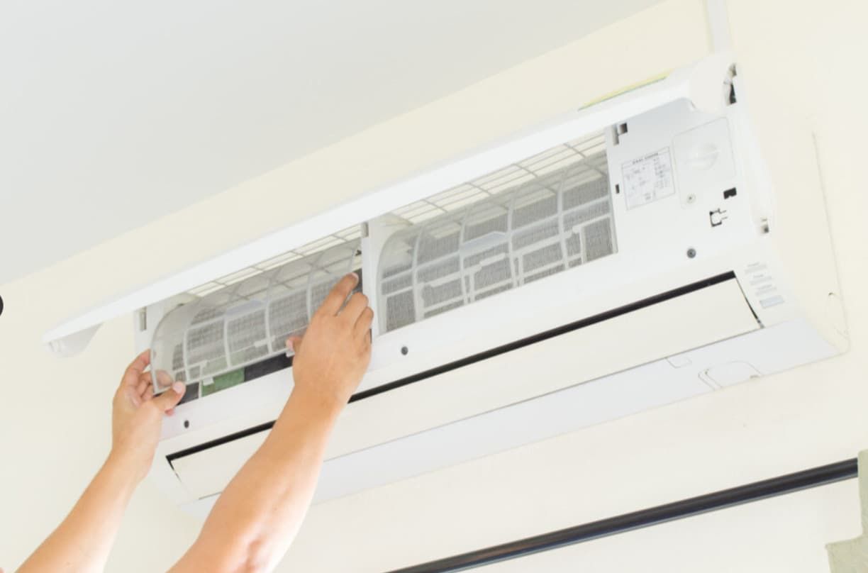A Person Is Cleaning A Wall Mounted Air Conditioner — Mozzlec Electrical & Airconditioning In Urangan, QLD