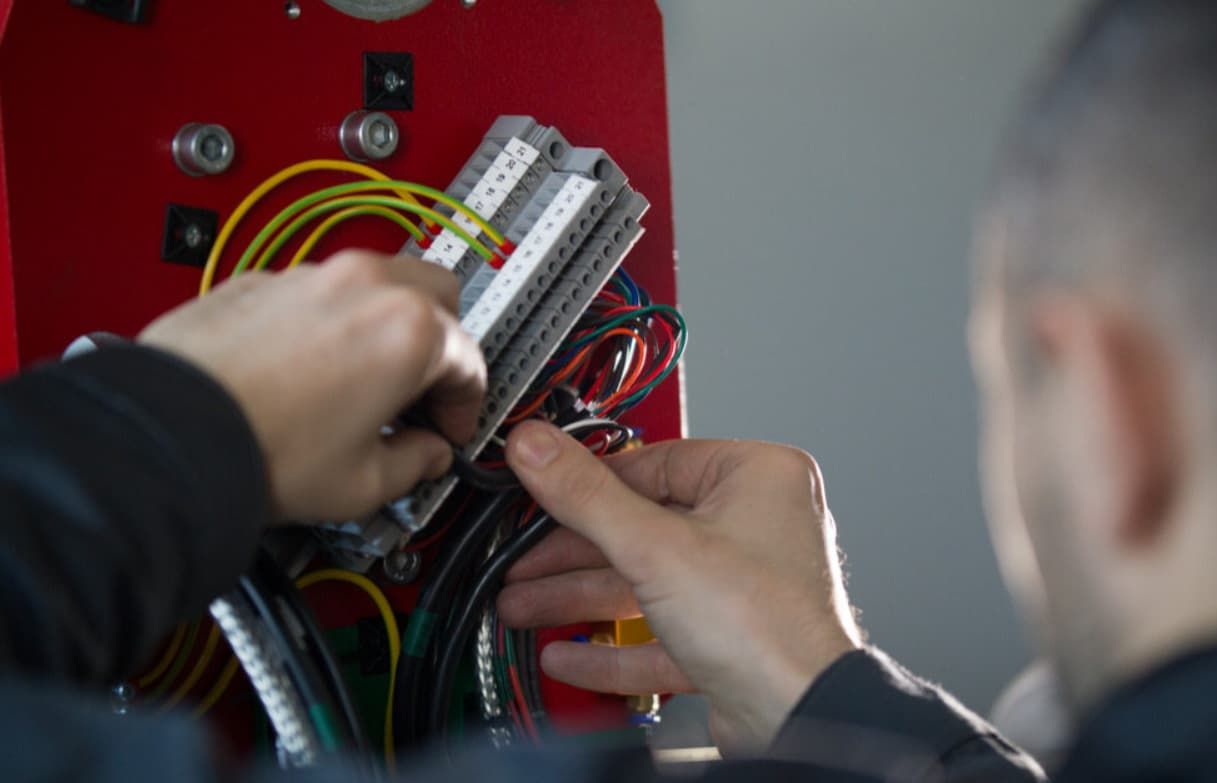 A Man Is Working On A Machine With Wires And A Screwdriver — Mozzlec Electrical & Airconditioning In Urangan, QLD