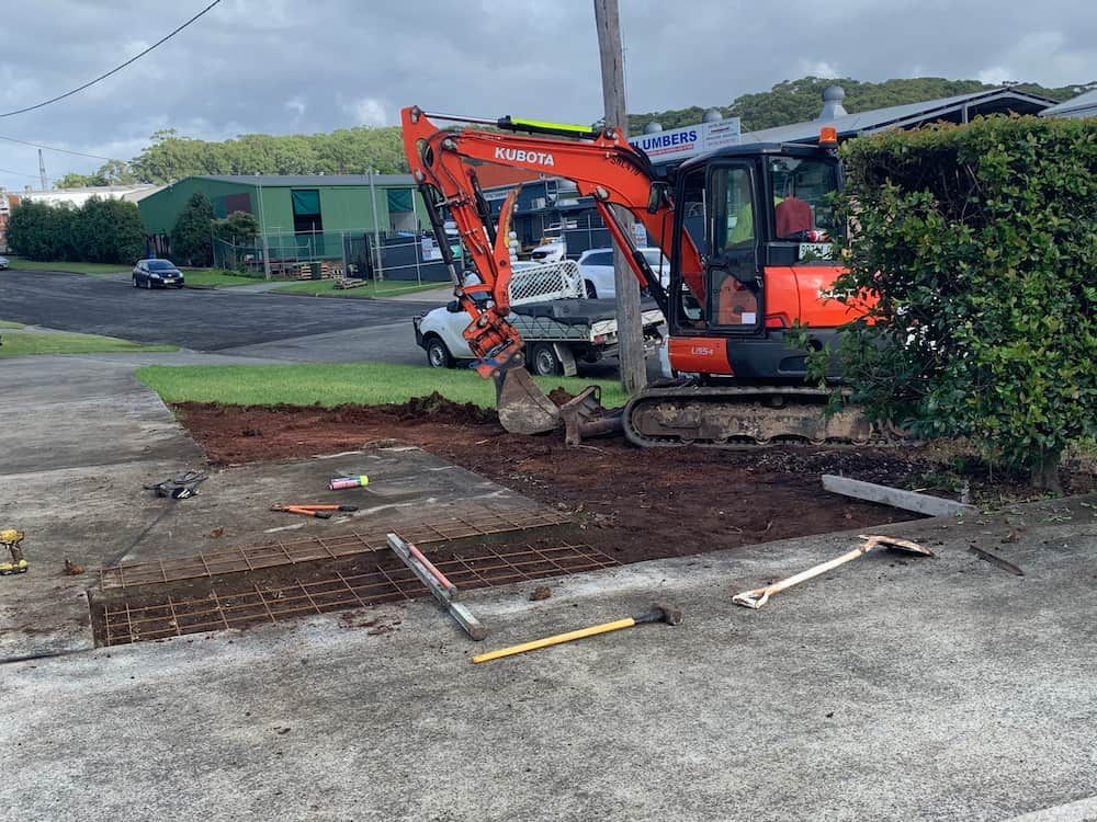 An Excavator Is Digging A Hole In The Ground In A Parking Lot — Brodie Wynter Concreting in Wauchope, NSW