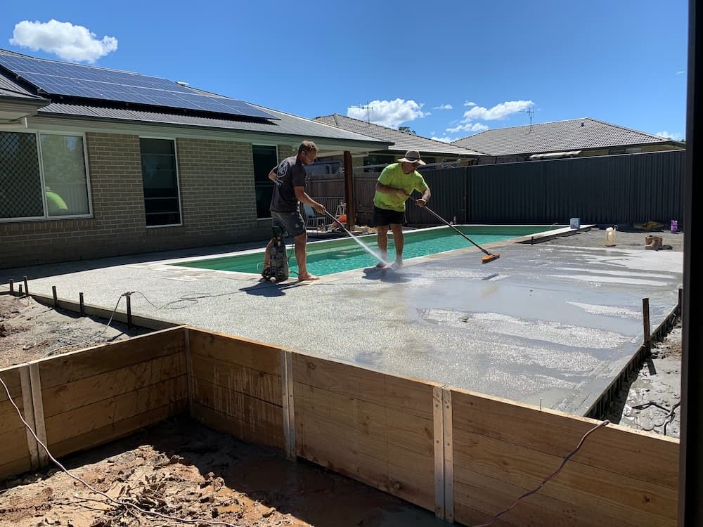 Two Men Are Working On A Concrete Deck In Front Of A Swimming Pool — Brodie Wynter Concreting in Coffs Harbour, NSW