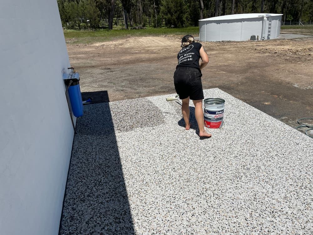 A Woman Is Standing On A Concrete Surface Next To A Bucket Of Paint  — Brodie Wynter Concreting in Macksville, NSW