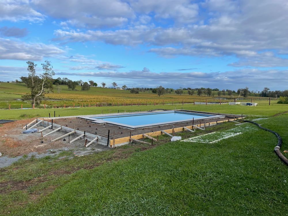 A Large Swimming Pool Is Being Built In The Middle Of A Grassy Field  — Brodie Wynter Concreting in Forster, NSW