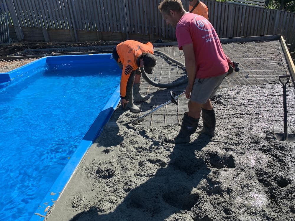 A Man In A Pink Shirt Is Standing Next To A Pool  — Brodie Wynter Concreting in Laurieton, NSW