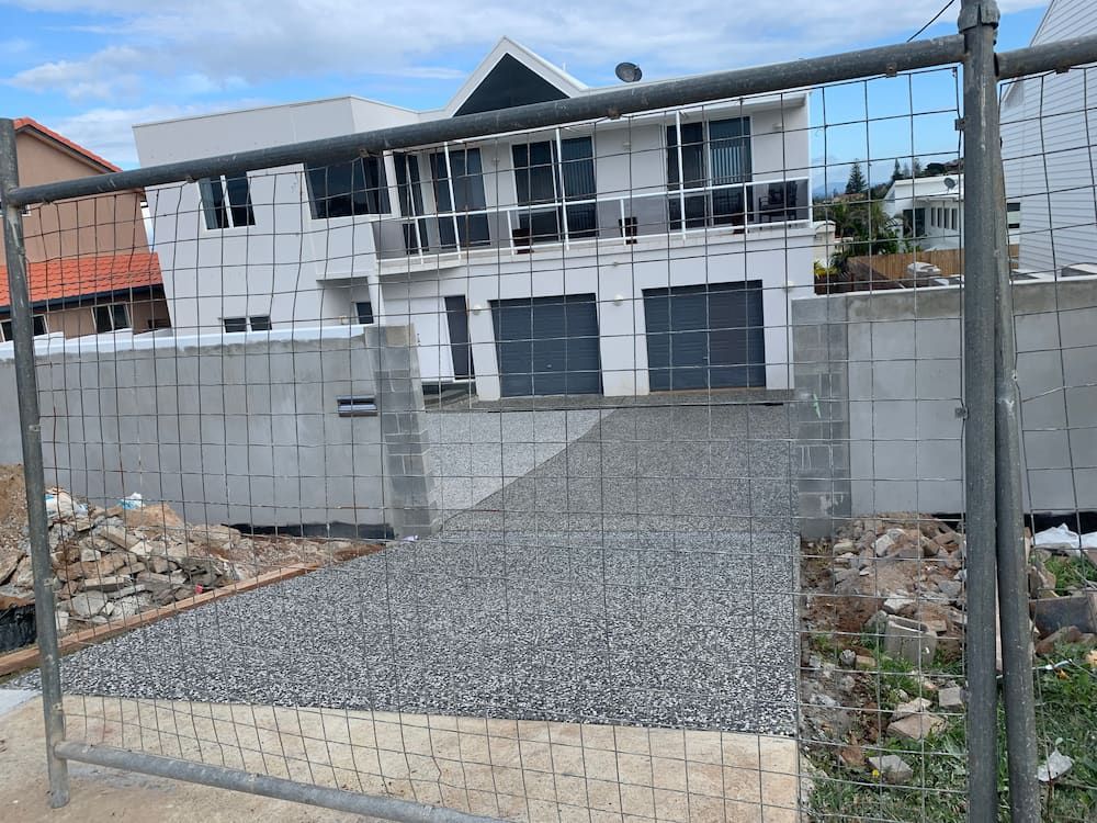 A Fence Is Surrounding A Construction Site With A House In The Background — Brodie Wynter Concreting in Port Macquarie, NSW