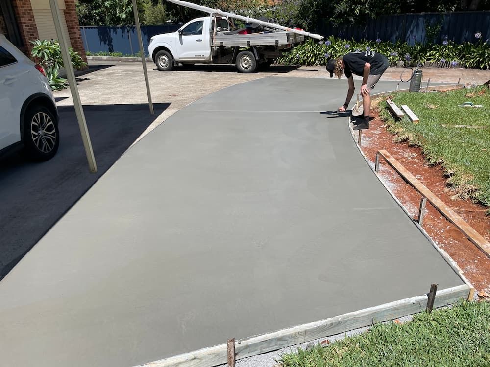 A Man Is Working On A Concrete Driveway In Front Of A White Truck  — Brodie Wynter Concreting in Port Macquarie, NSW