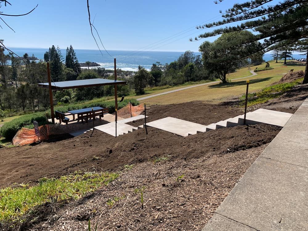 A Picnic Table Is Sitting On Top Of A Dirt Hill Overlooking The Ocean  — Brodie Wynter Concreting in Port Macquarie, NSW