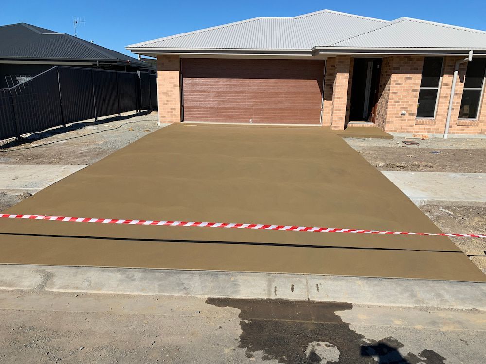 A Brick House With A Brown Garage Door And A Concrete Driveway — Brodie Wynter Concreting in Port Macquarie, NSW