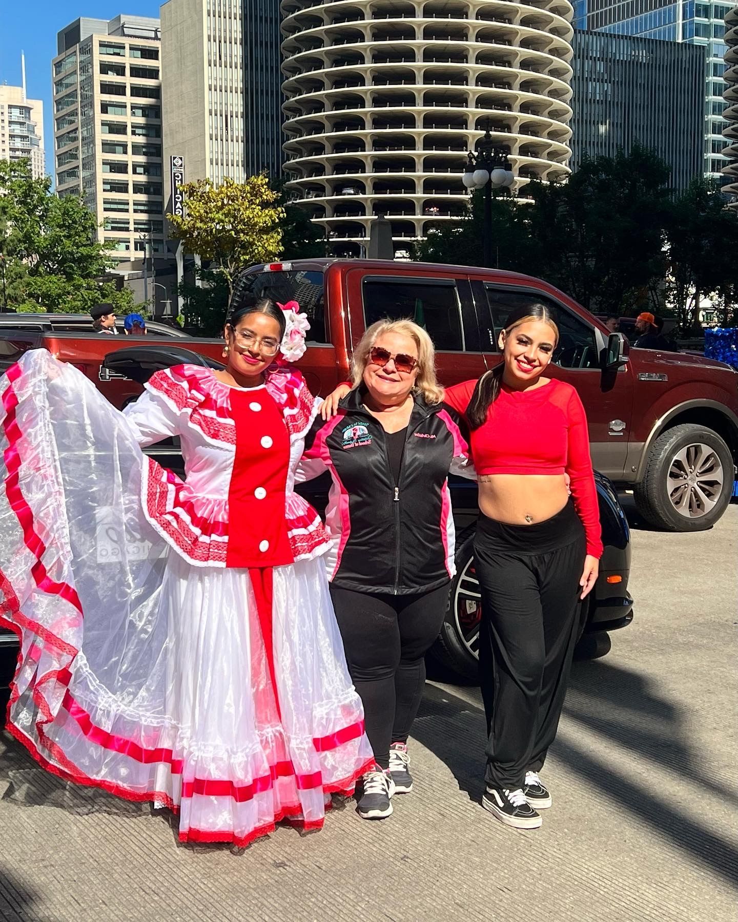 Three women are posing for a picture in front of a car in a parking lot.