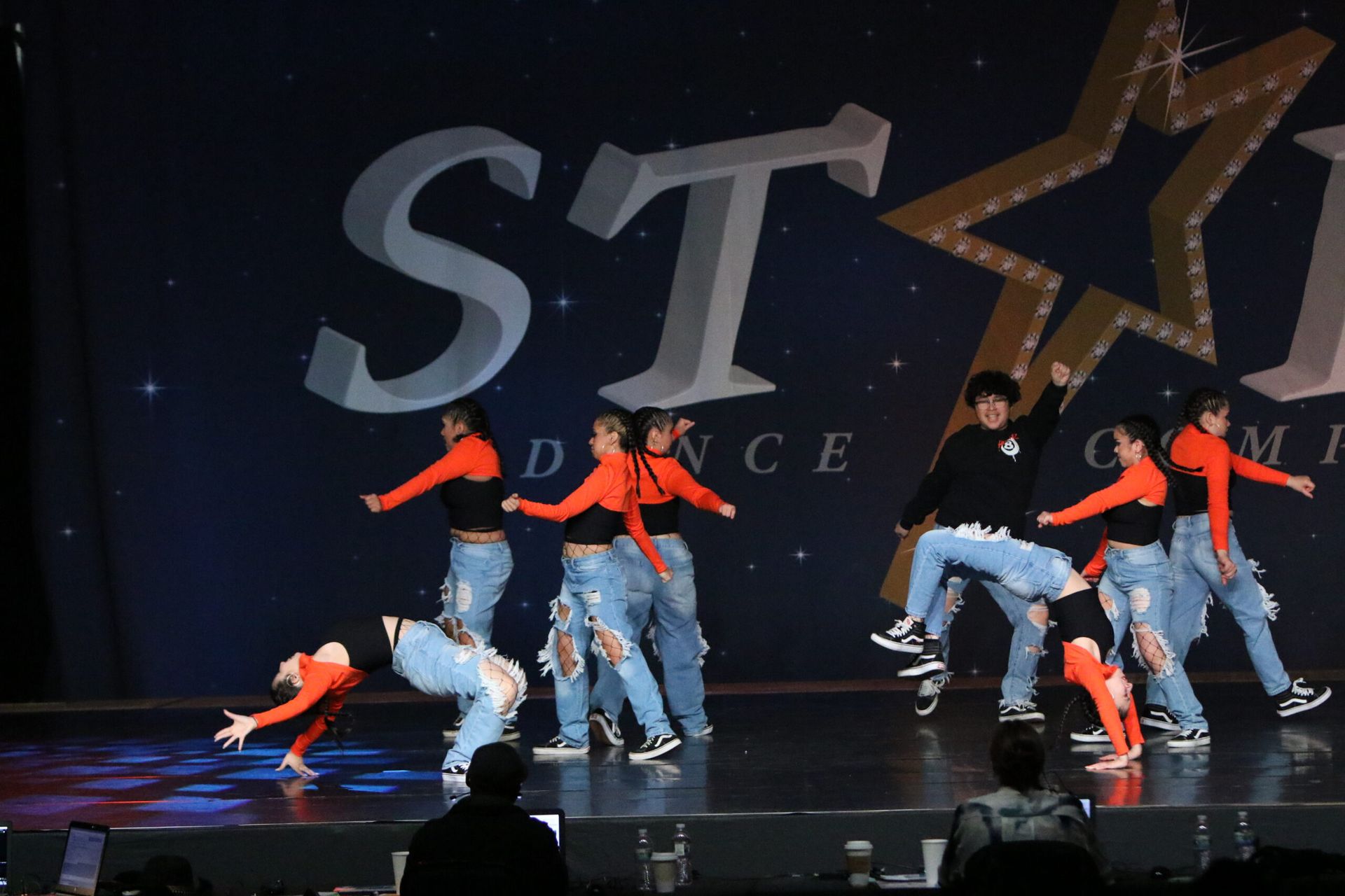 A group of dancers are performing on a stage in front of a sign that says st dance