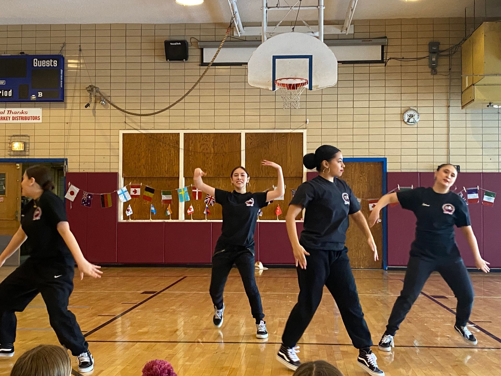 A group of people are dancing in a gym with a basketball hoop in the background