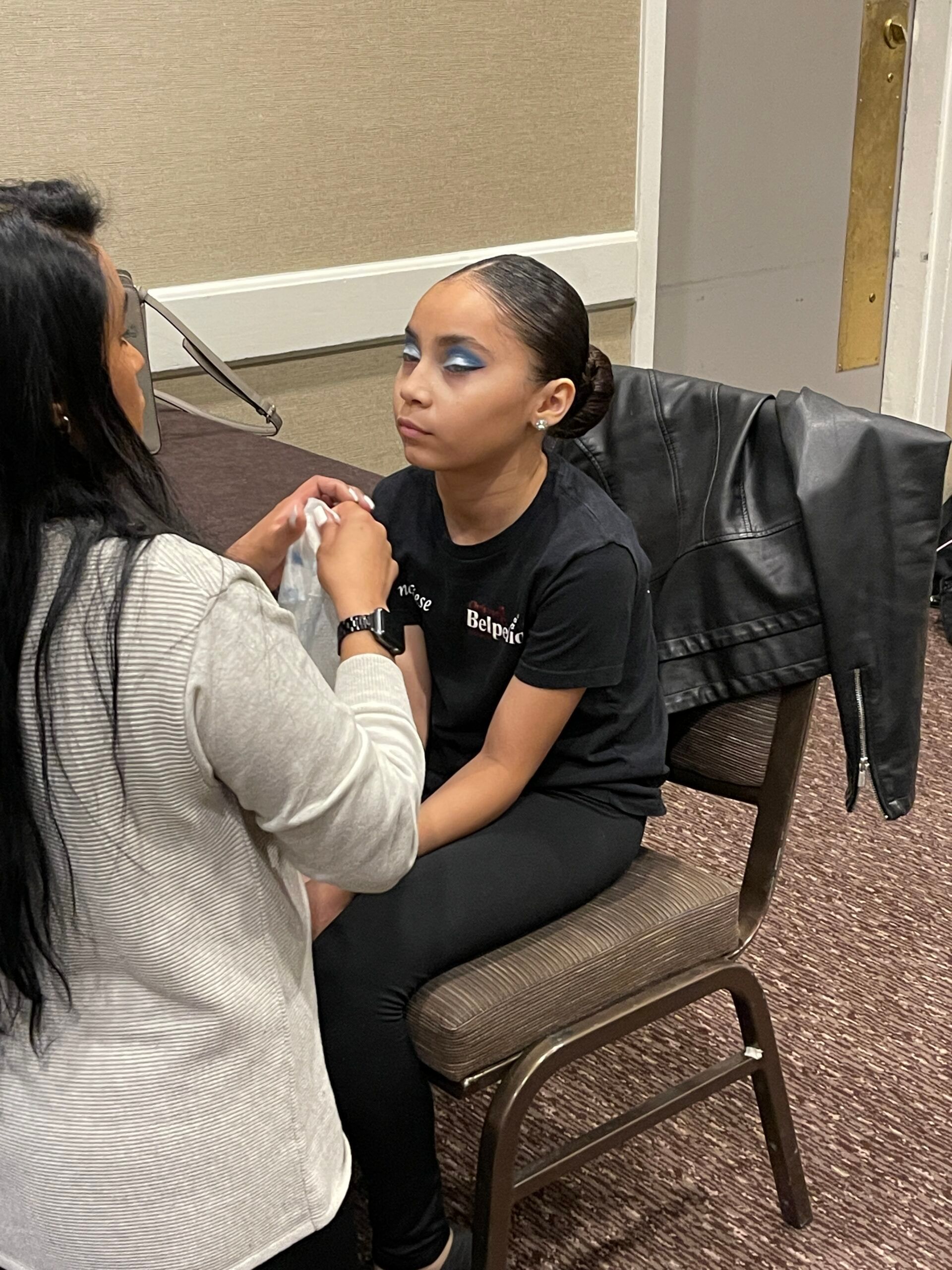 A woman is applying makeup to a young girl who is sitting in a chair.