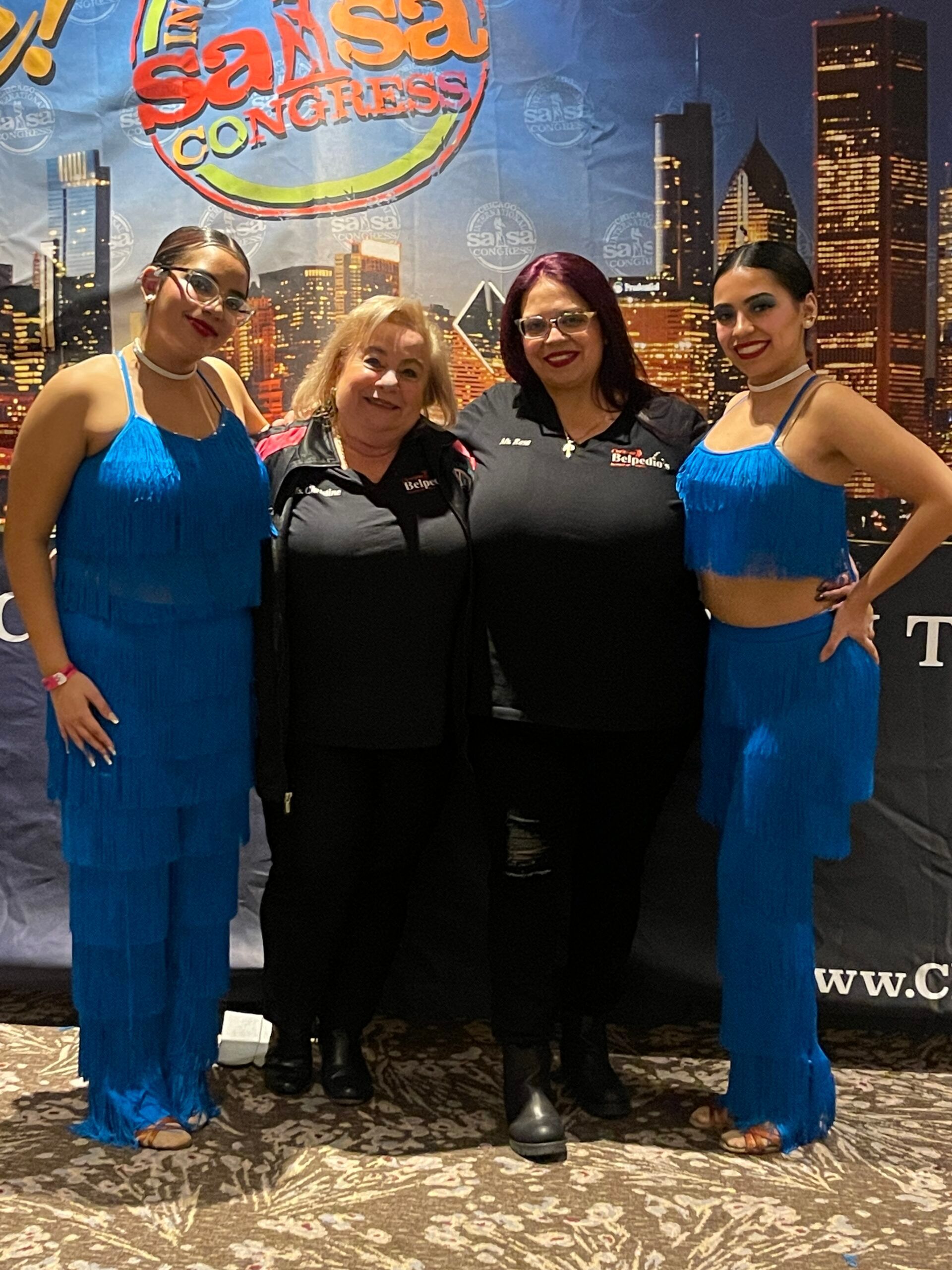Four women are posing for a picture in front of a sign that says salsa congress