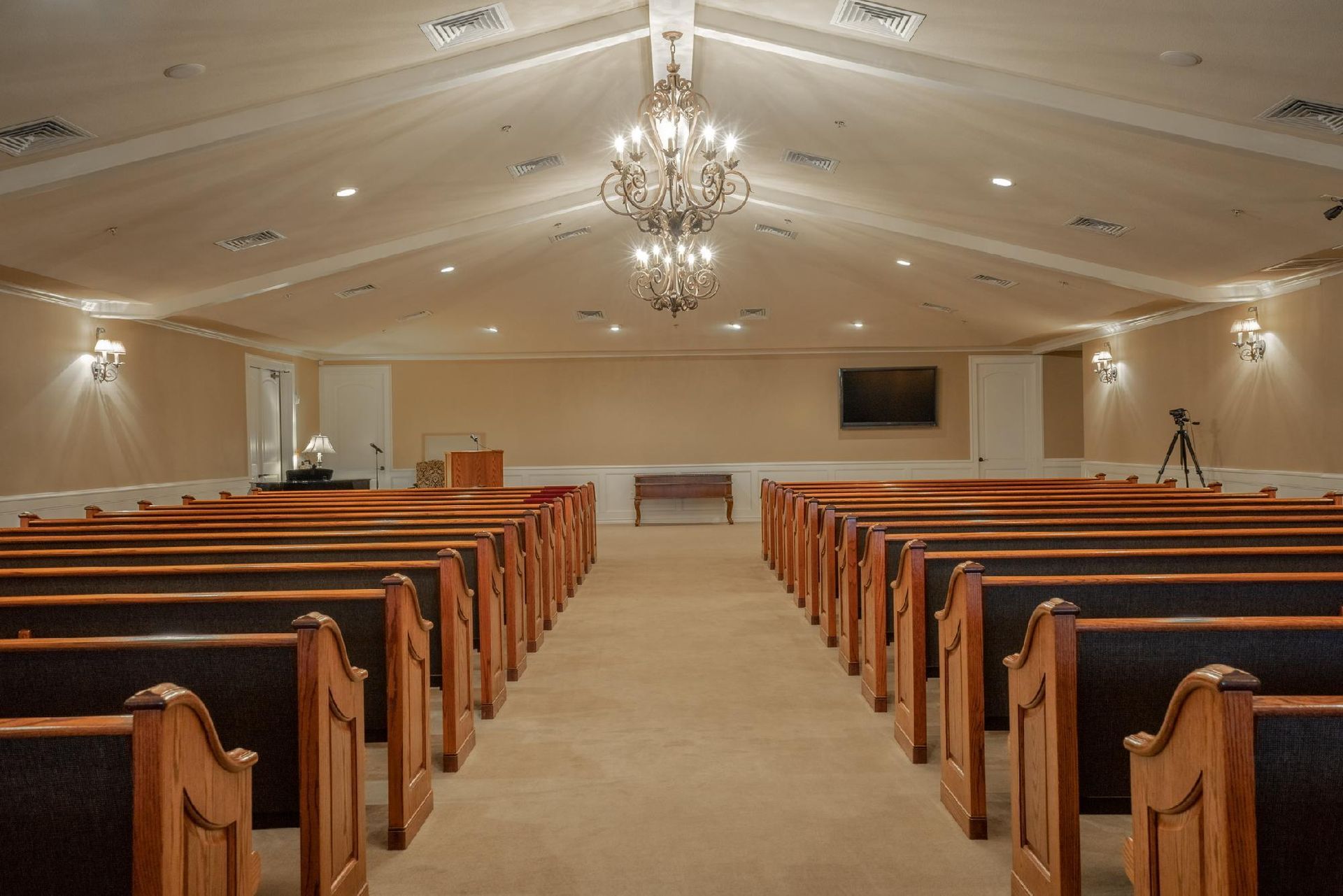 Interior view of a chapel with rows of wooden pews, chandelier, and a raised platform.