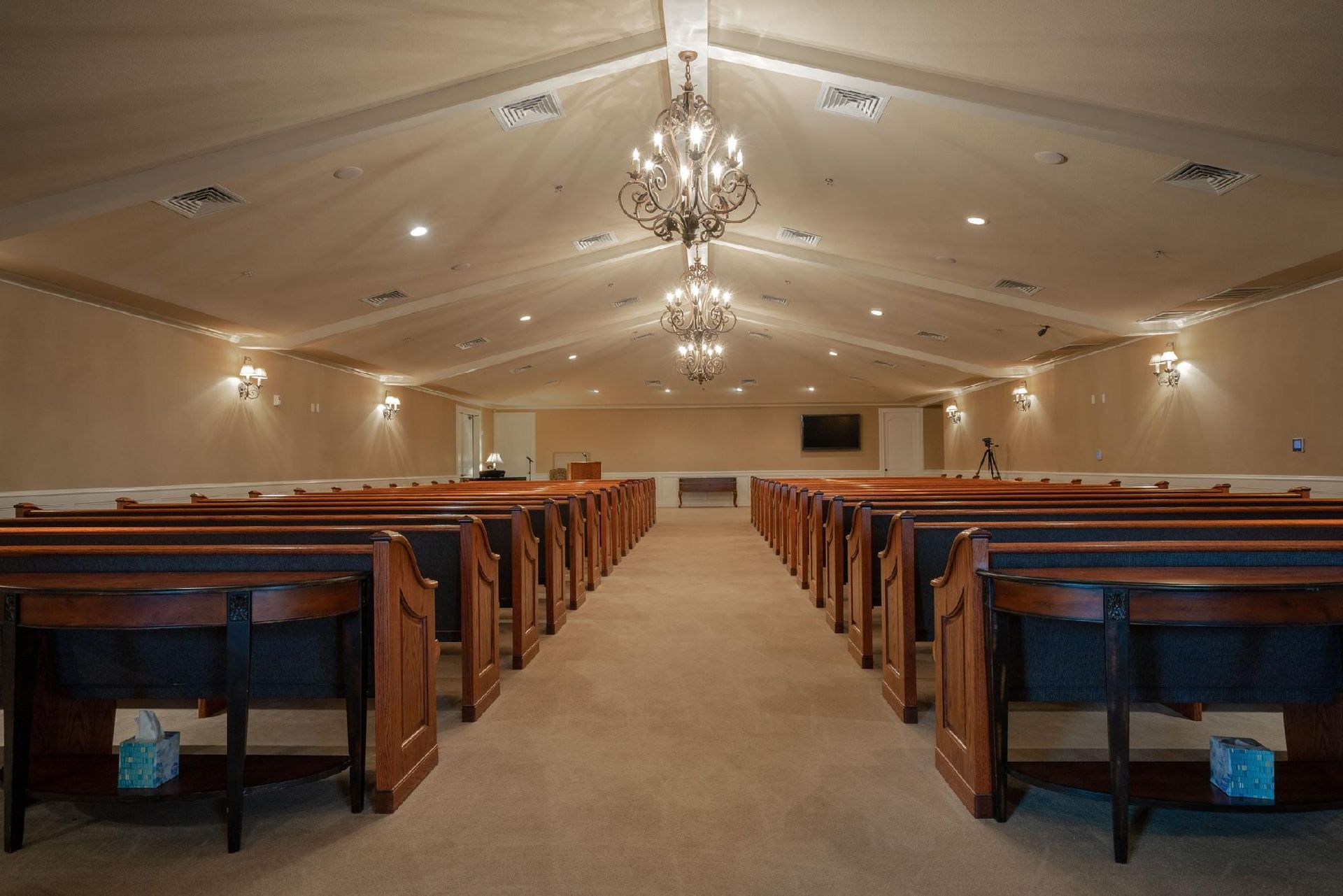 Funeral home interior with pews, chandeliers, and a central aisle.