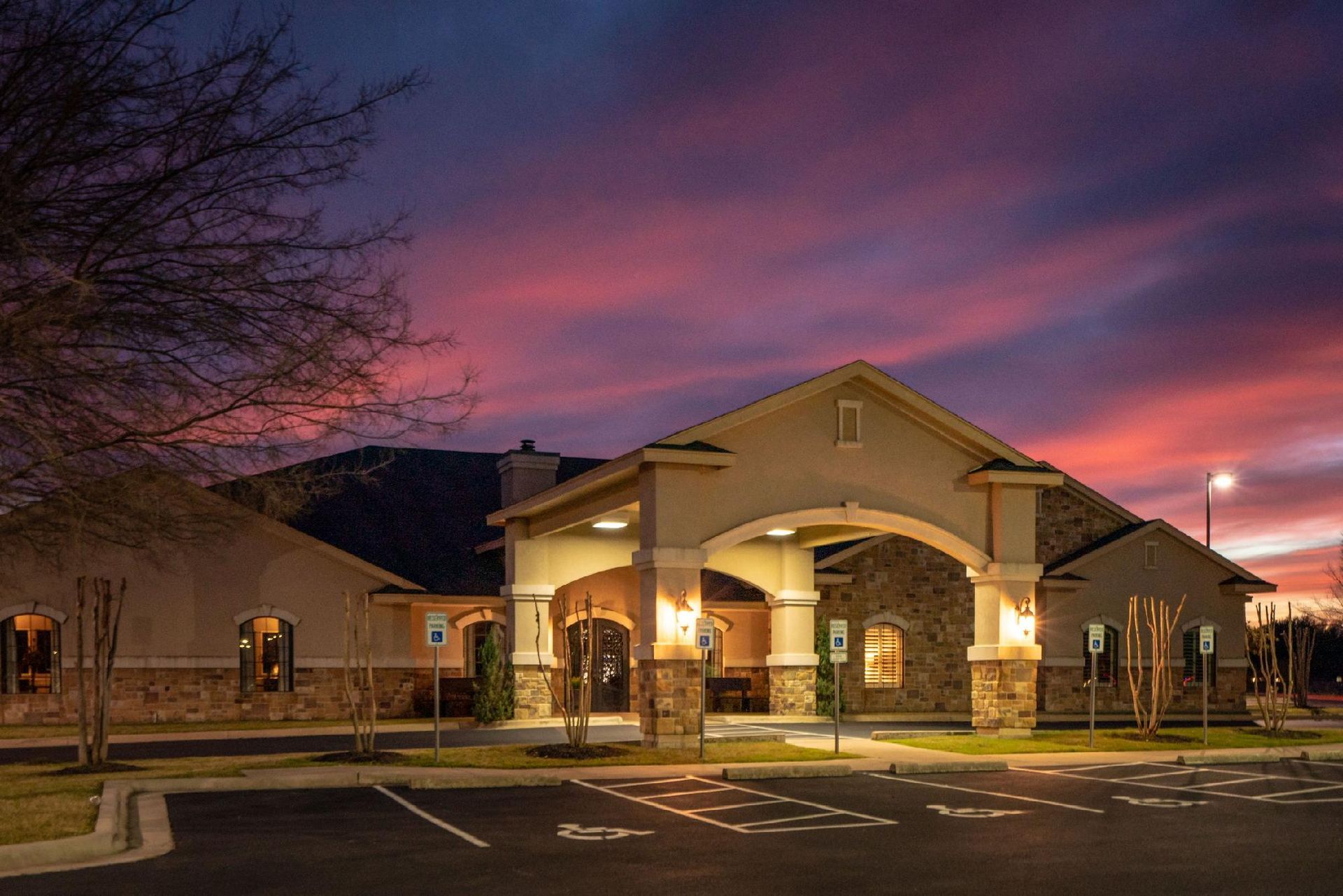 Building exterior at dusk with an arched entrance, lit up, under a colorful sunset sky.