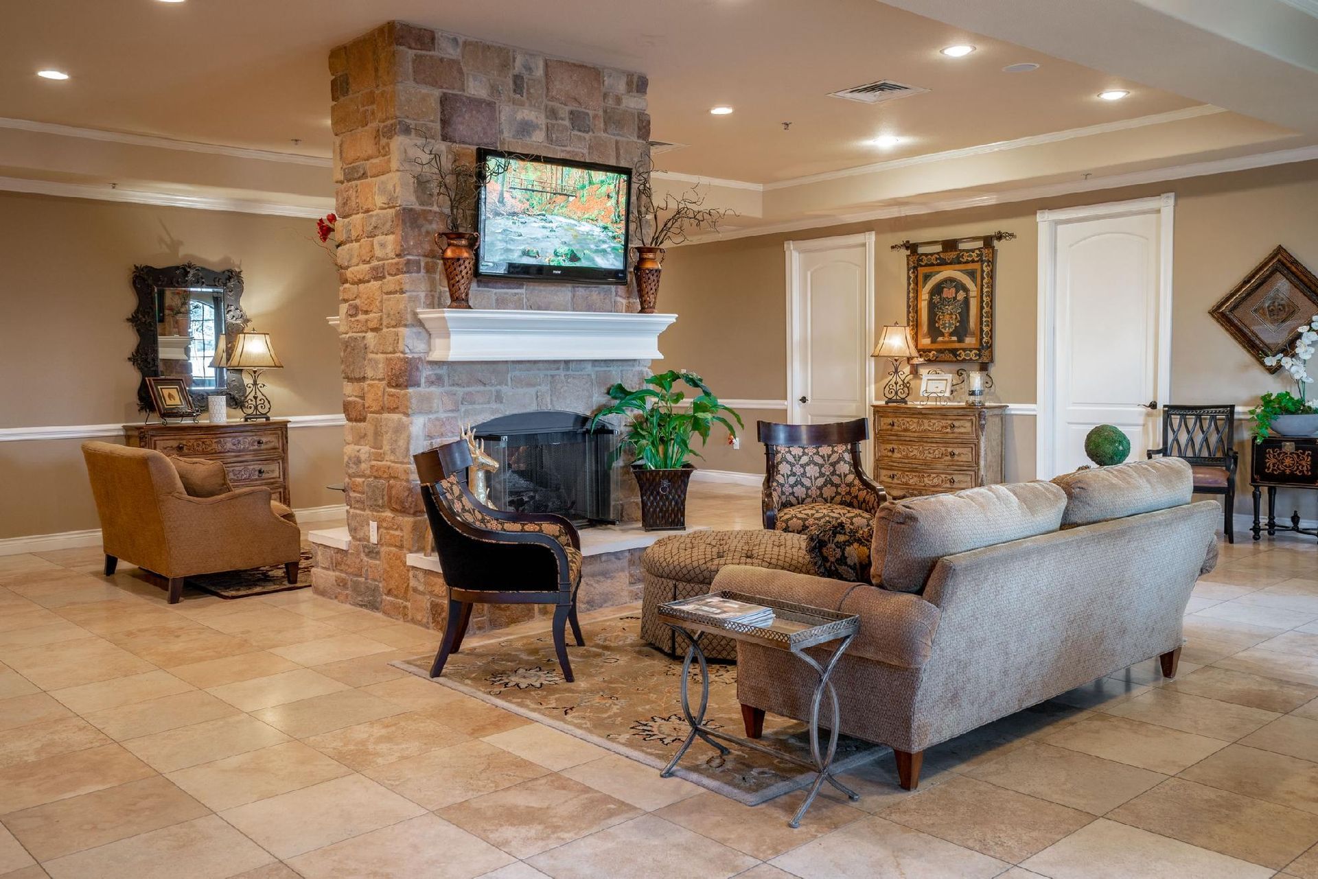 Cozy living room with fireplace, TV, and seating area. Beige and brown tones with light stone and marble flooring.