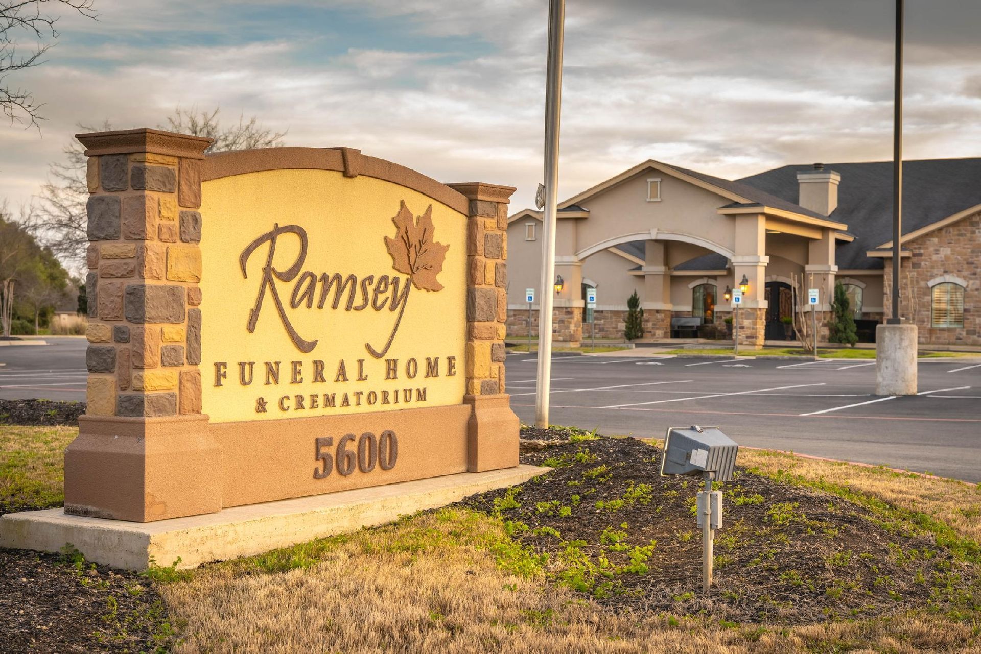 Sign for Ramsey Funeral Home & Crematory, a tan building is in the background. The sign is brown and beige.