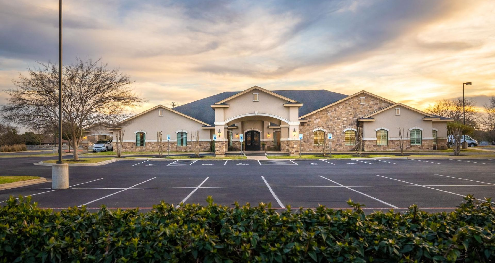 Building with beige exterior, stone accents, parking lot, and cloudy sunset.