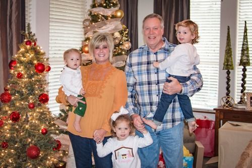 Family poses in front of Christmas tree: adults holding young children.