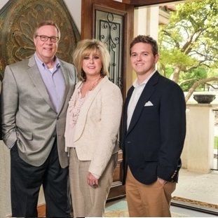 Three people standing in a doorway. Man in gray suit, woman in cream blazer, and man in navy blazer.