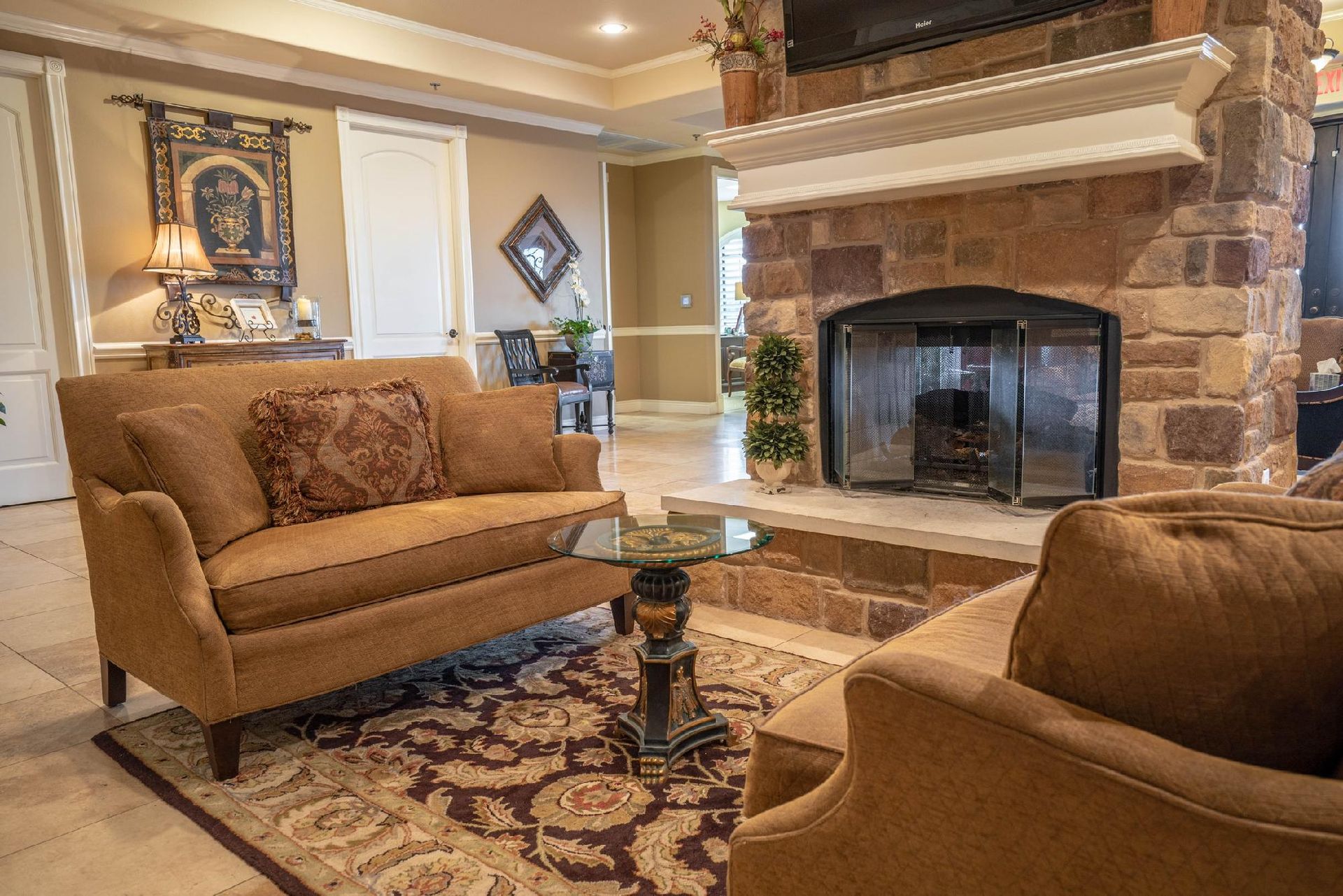 Living room with stone fireplace, brown furniture, ornate rug, and glass-top table.