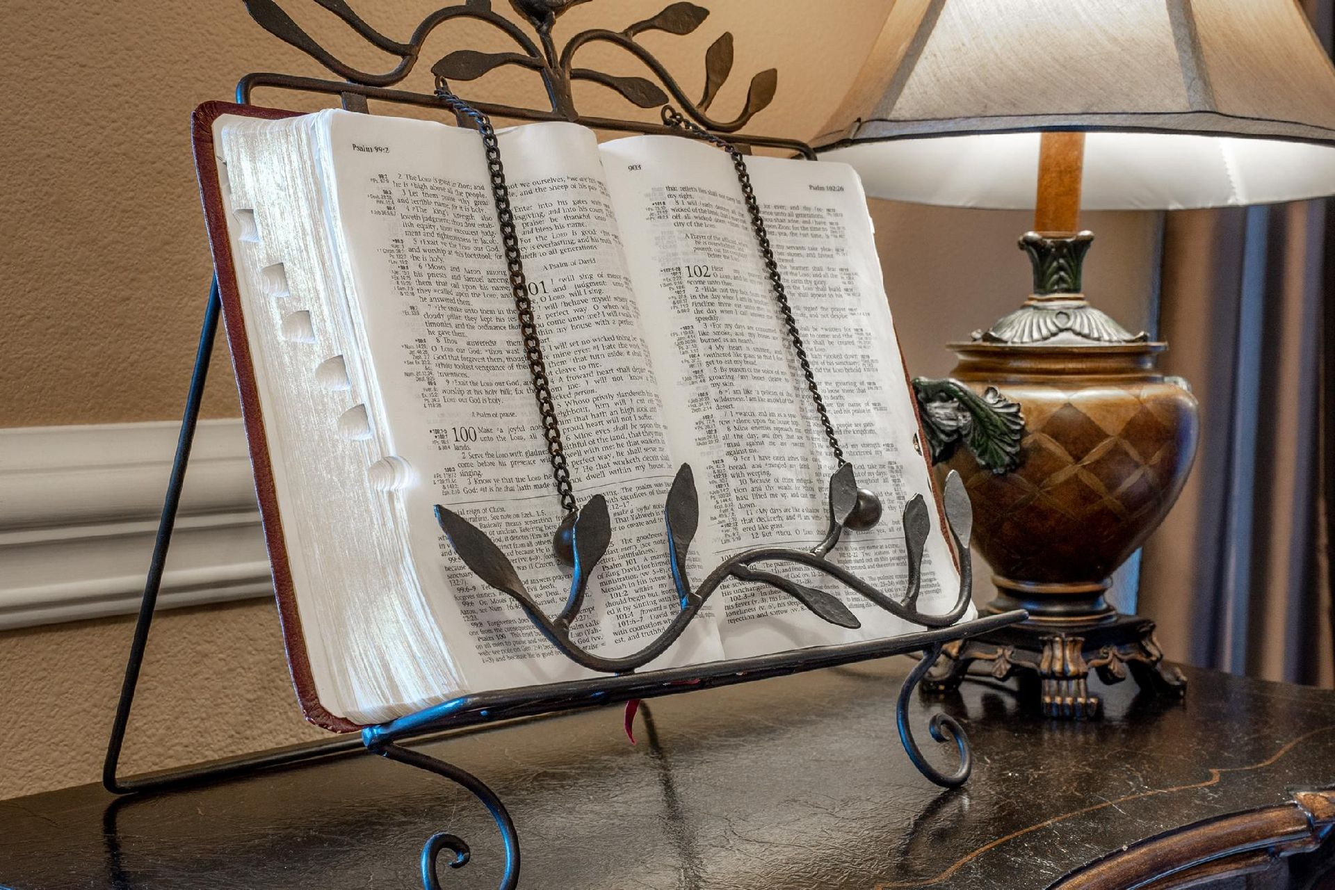 Large open book on a decorative stand next to a lit lamp.